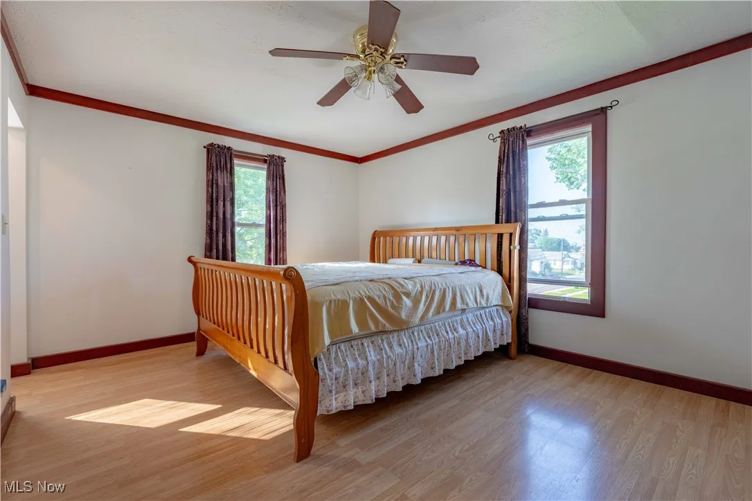 Bedroom featuring multiple windows, light wood-style flooring, crown molding, and a ceiling fan