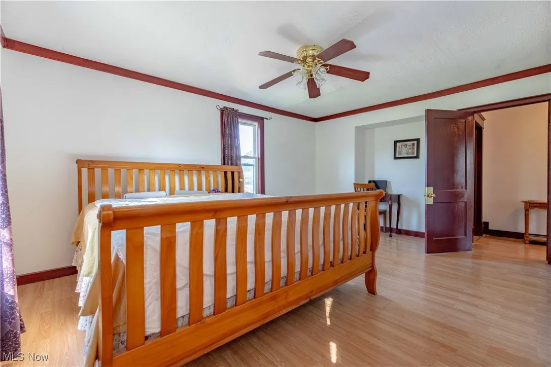 Bedroom with light wood finished floors, ornamental molding, and a ceiling fan