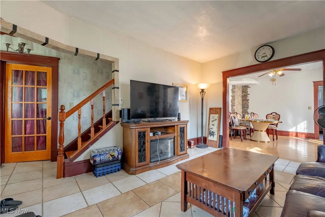 Living room featuring ceiling fan, tile patterned flooring, and stairway