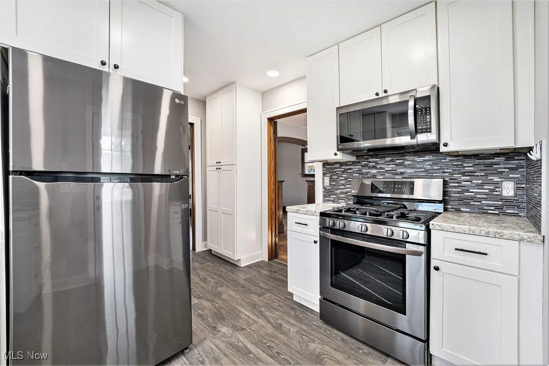 Kitchen with appliances with stainless steel finishes, dark wood finished floors, backsplash, white cabinets, and recessed lighting