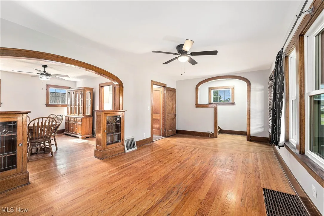 Living area with a ceiling fan, light wood-style floors, and arched walkways