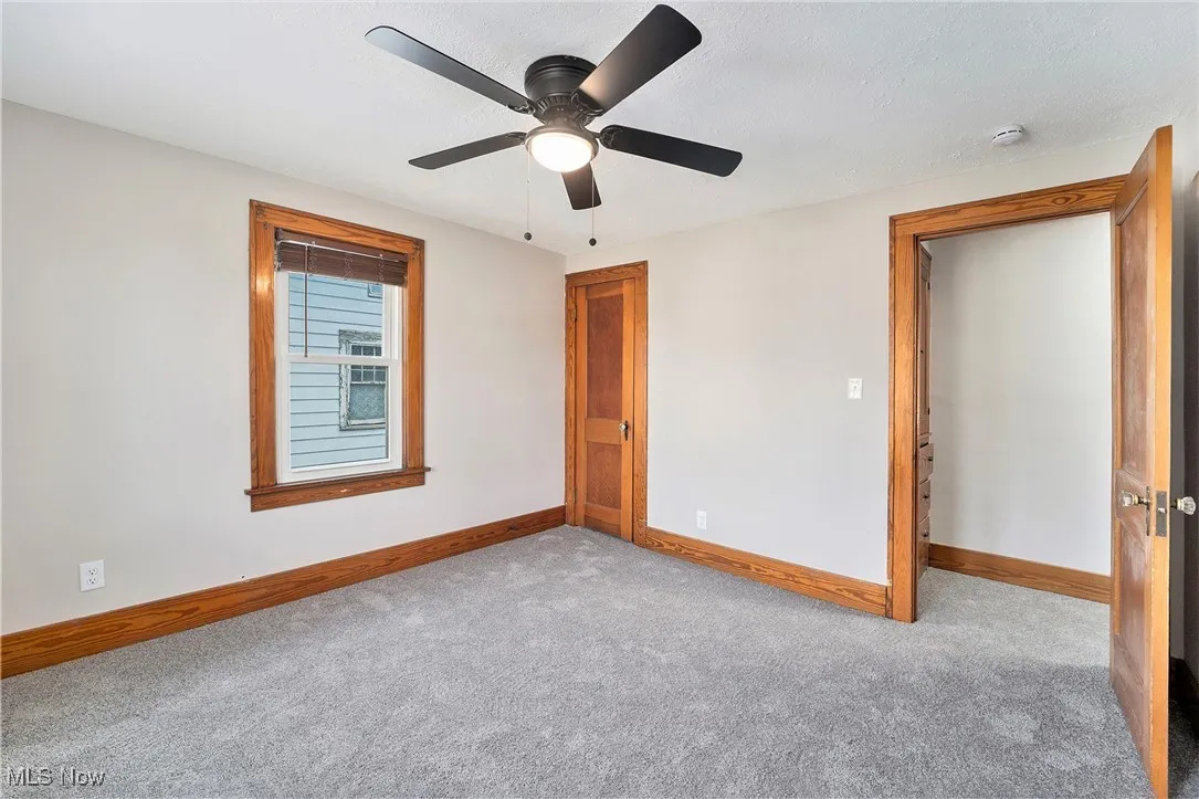 Carpeted empty room with a smoke detector and ceiling fan