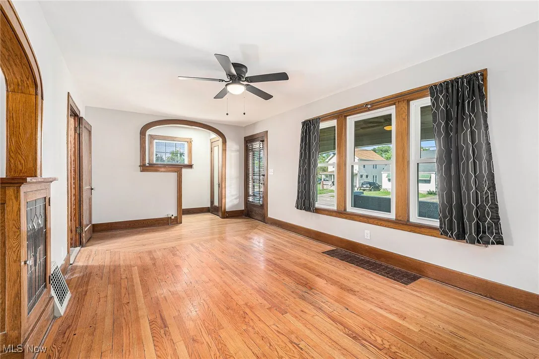 Unfurnished living room with arched walkways, light wood finished floors, and ceiling fan