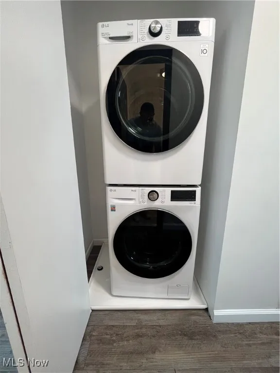 Washroom with stacked washer / drying machine and wood finished floors
