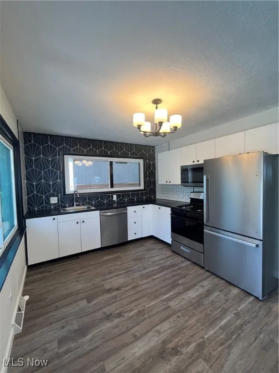 Kitchen with fridge, range, dishwashing machine, dark countertops, and a chandelier