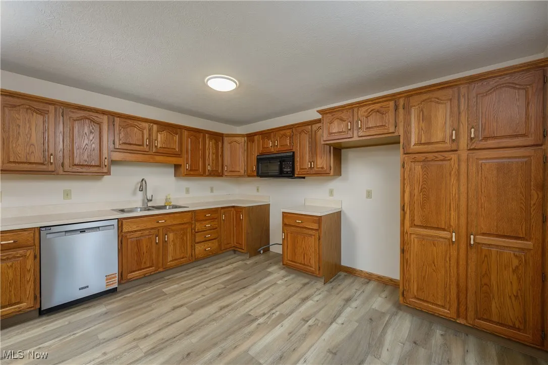 Kitchen with dishwasher, black microwave, brown cabinetry, and light wood-style flooring