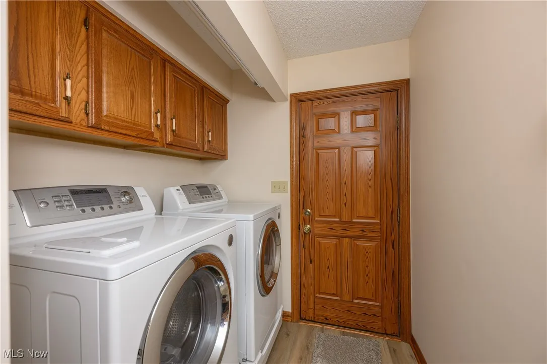 Laundry area featuring washer and clothes dryer, light wood-type flooring, cabinet space, and a textured ceiling