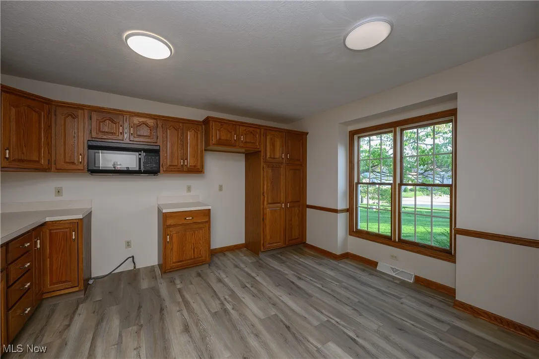 Kitchen featuring black microwave, brown cabinetry, light wood-style floors, and light countertops