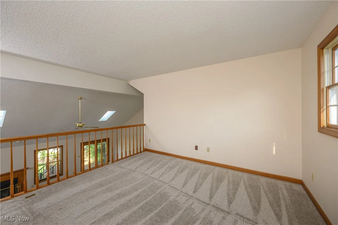 Carpeted empty room featuring ceiling fan, plenty of natural light, a textured ceiling, and a skylight