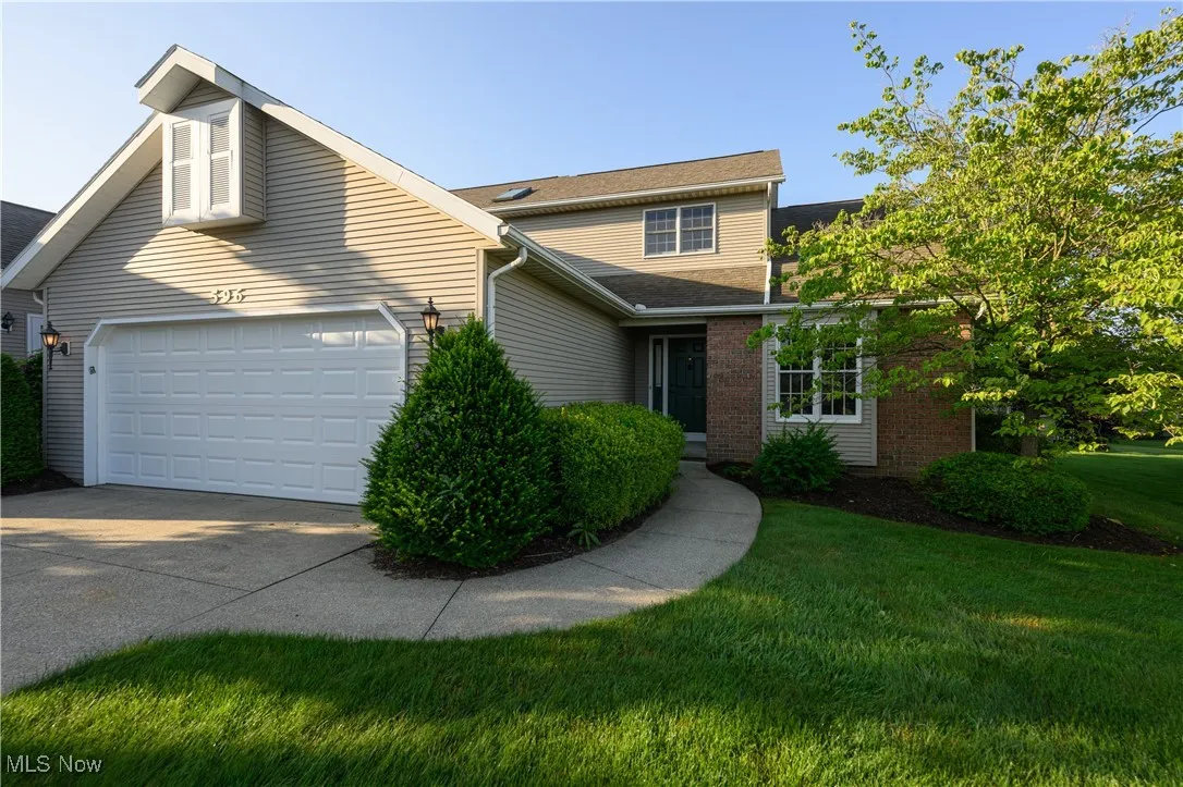 Traditional home featuring a garage, driveway, a front yard, brick siding, and roof with shingles
