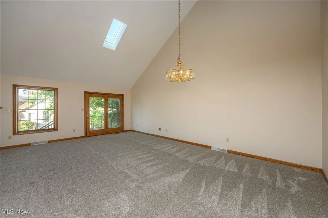 Carpeted spare room featuring a skylight, high vaulted ceiling, and a chandelier