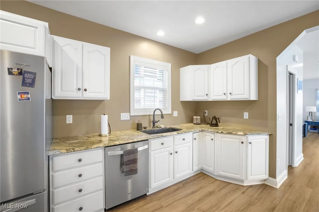 Kitchen featuring appliances with stainless steel finishes, light wood-type flooring, light stone countertops, white cabinetry, and recessed lighting