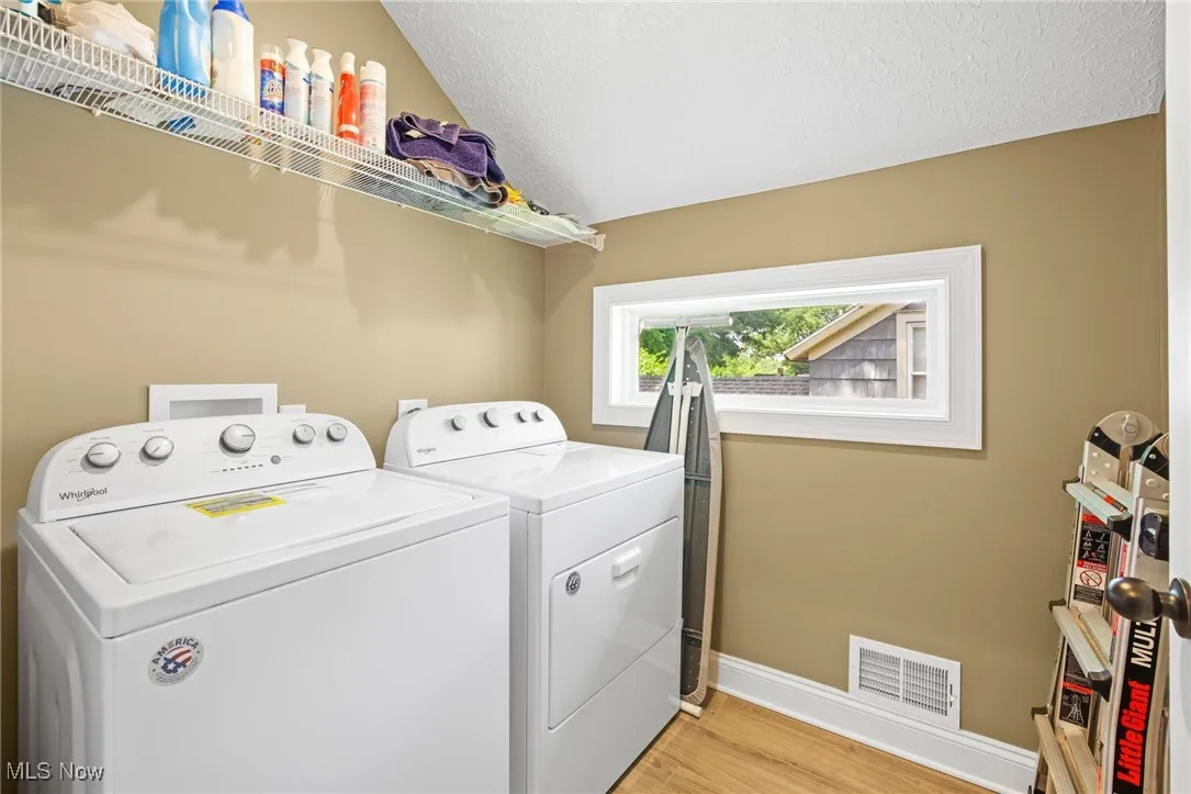 Laundry area featuring washing machine and dryer, light wood-style flooring, and a textured ceiling