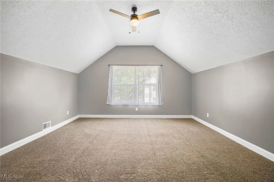 Additional living space featuring carpet flooring, a textured ceiling, ceiling fan, and lofted ceiling