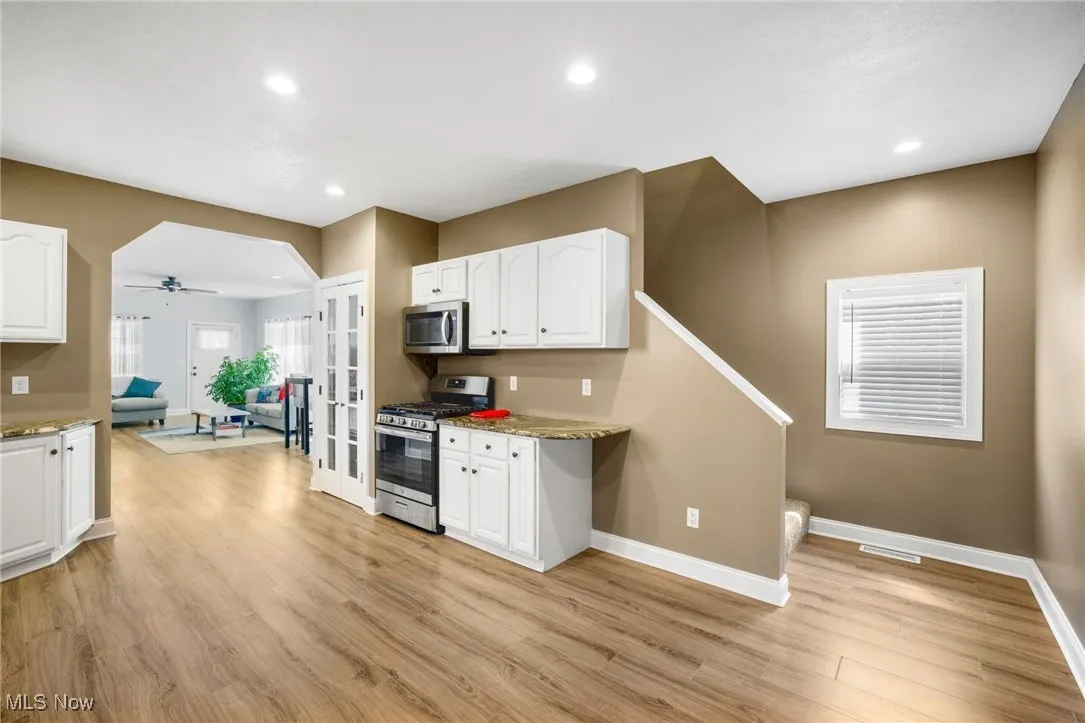 Kitchen with stainless steel appliances, white cabinetry, light wood-style floors, light stone counters, and recessed lighting