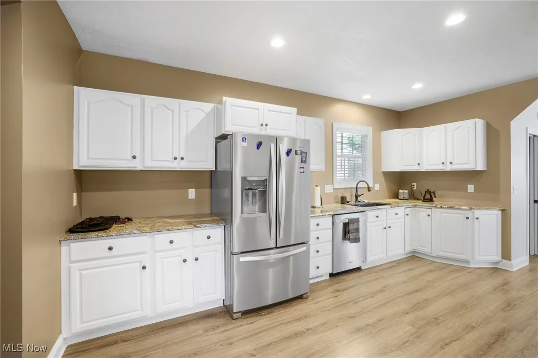 Kitchen featuring appliances with stainless steel finishes, light wood-type flooring, white cabinets, light stone counters, and recessed lighting