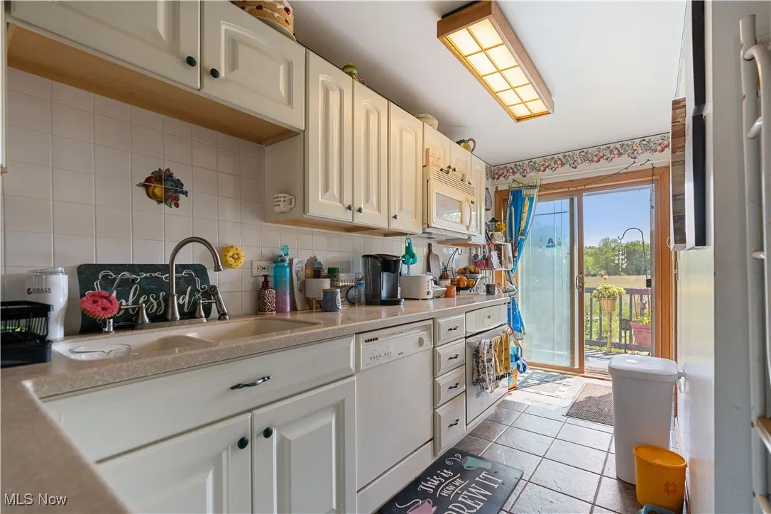 Kitchen with white appliances, decorative backsplash, light countertops, and tile patterned floors