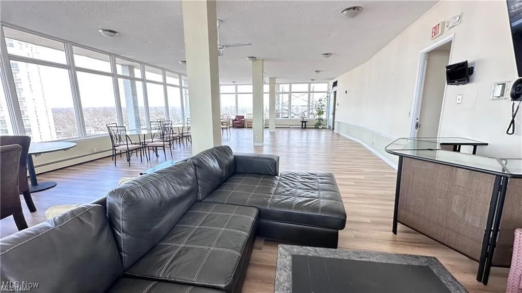 Living area featuring wood finished floors, healthy amount of natural light, a textured ceiling, a baseboard heating unit, and a ceiling fan