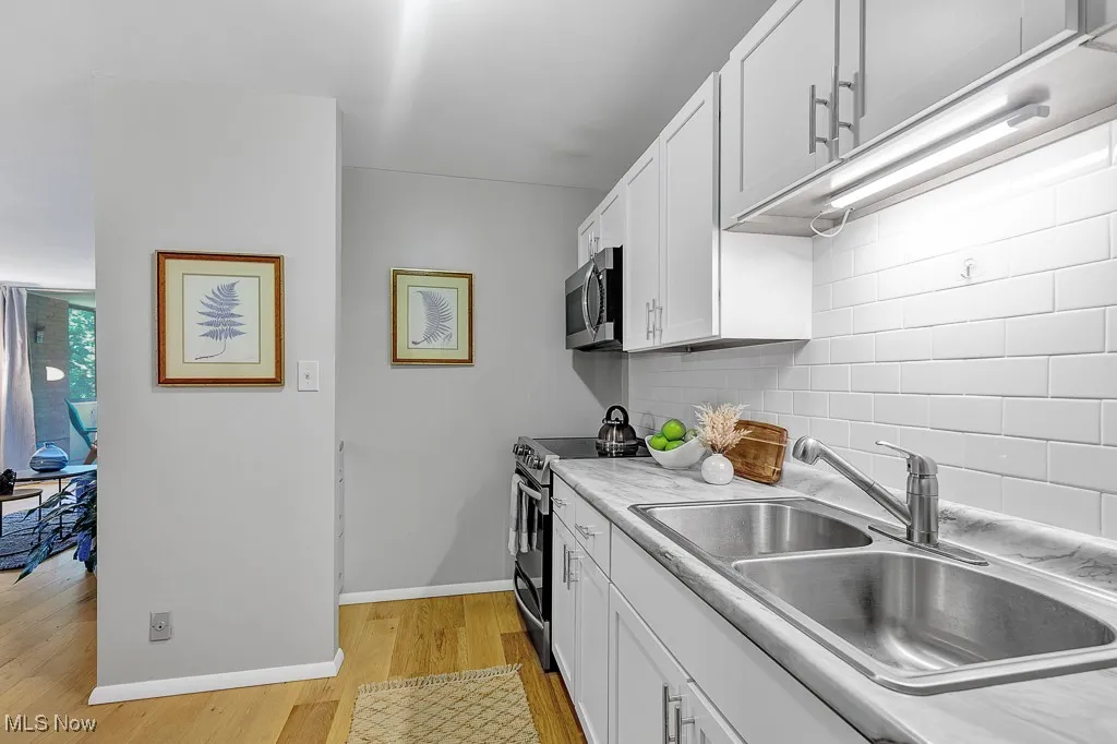 Kitchen featuring stainless steel appliances, light wood-style floors, tasteful backsplash, white cabinets, and light countertops