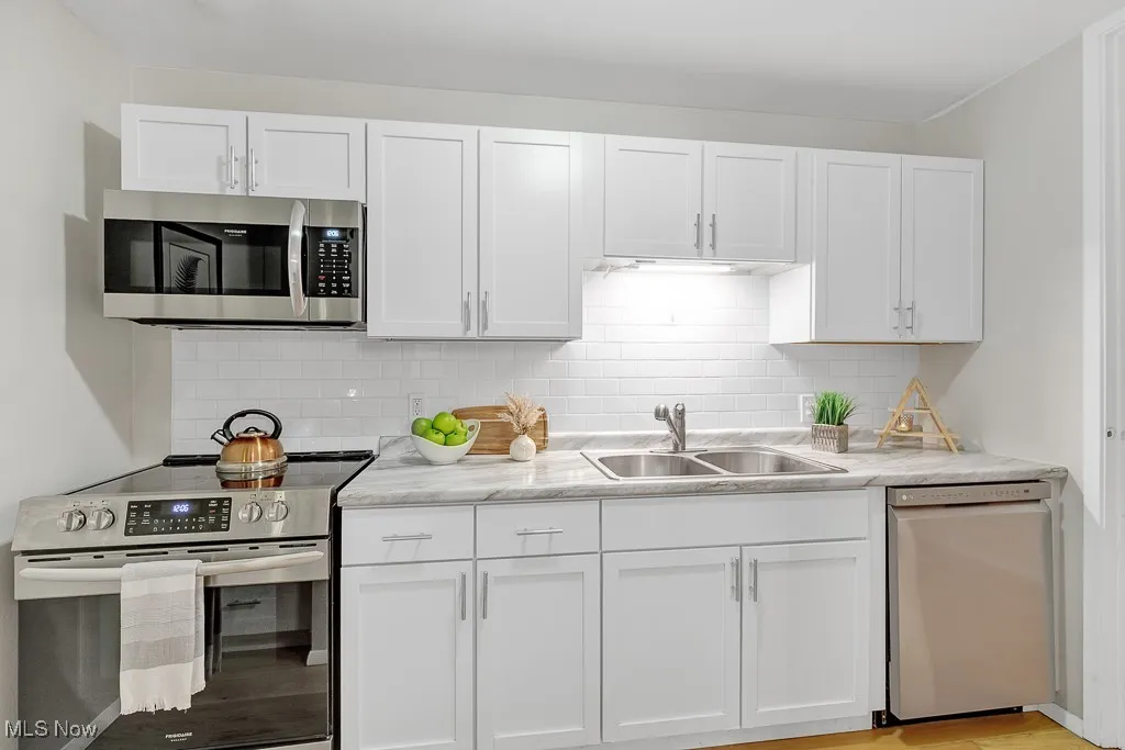 Kitchen with appliances with stainless steel finishes, white cabinetry, tasteful backsplash, and light wood-style flooring