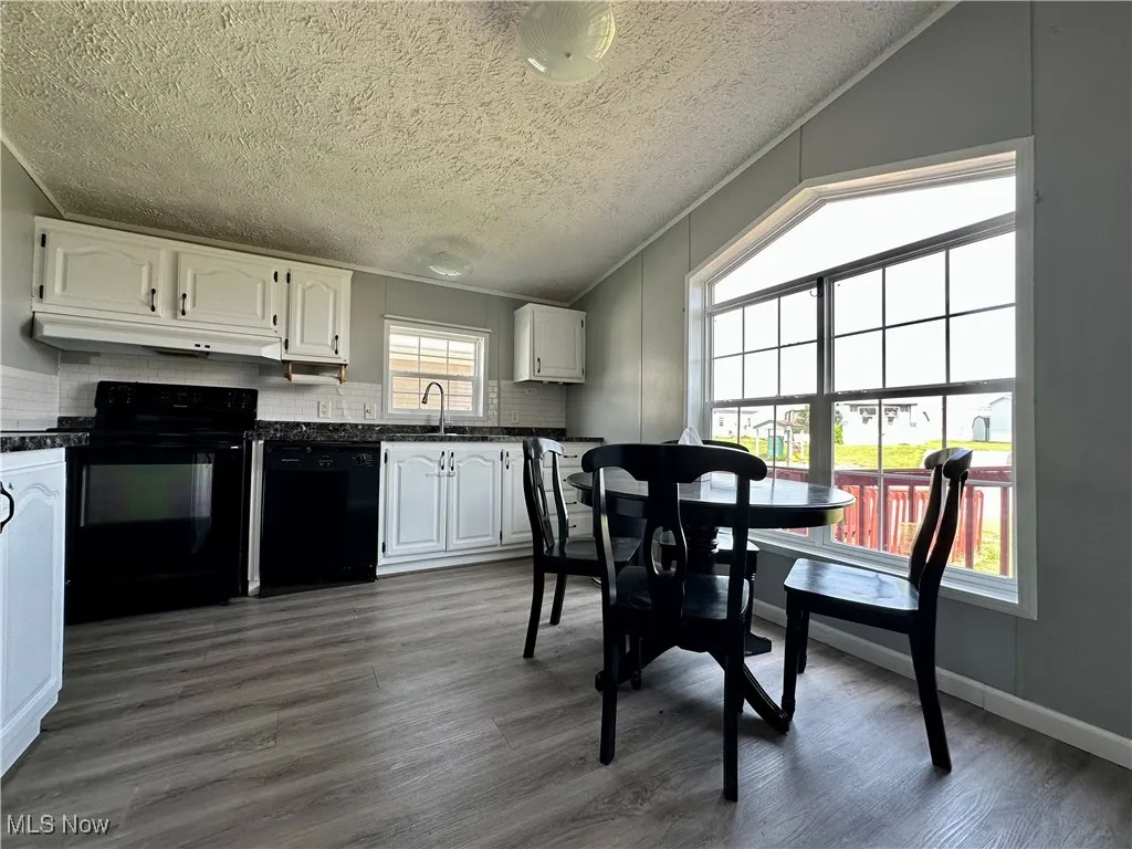 Kitchen featuring black appliances, under cabinet range hood, dark countertops, a sink, and white cabinets
