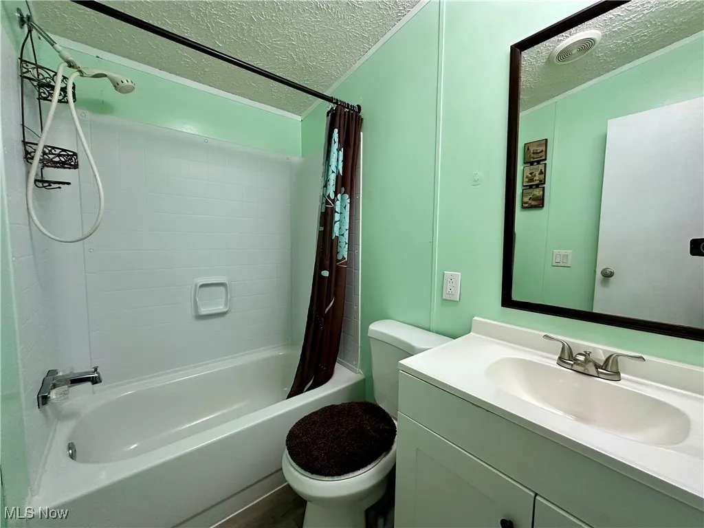 Full bath with a textured ceiling, shower / tub combo, toilet, and vanity