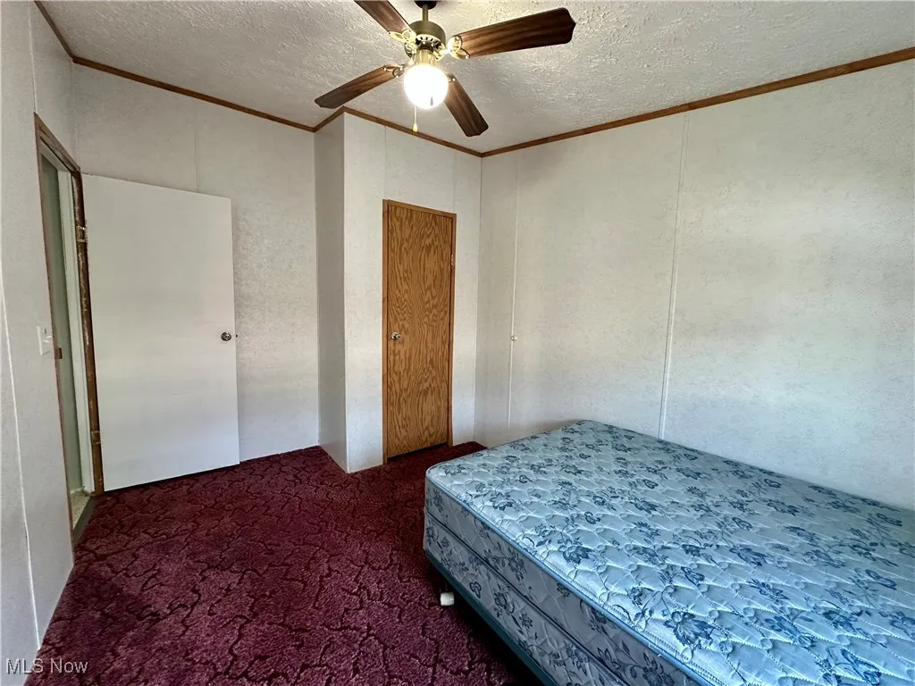 Bedroom featuring ornamental molding, a textured ceiling, carpet flooring, and a ceiling fan