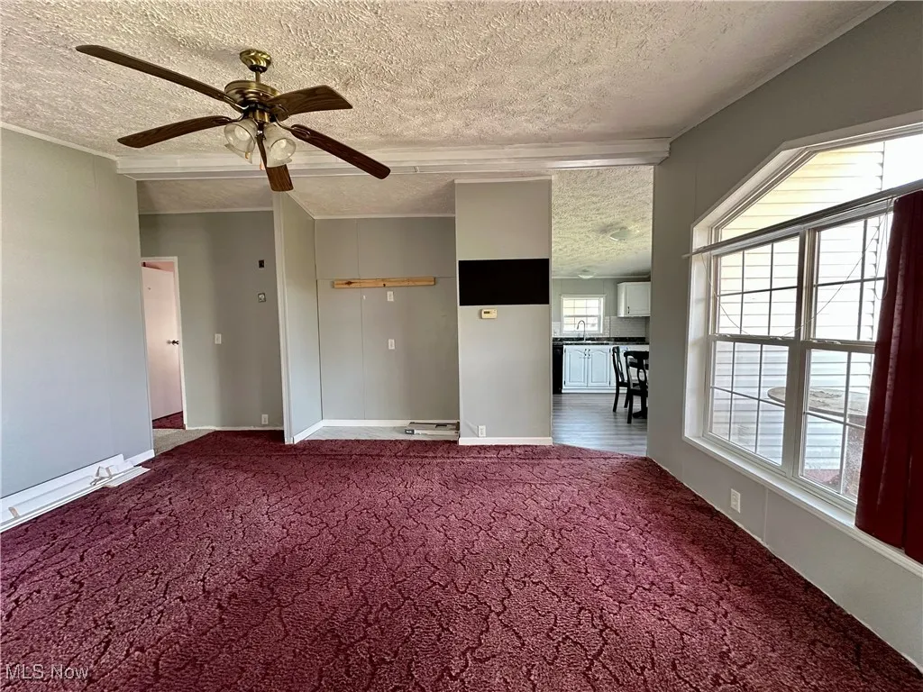 Carpeted spare room with a textured ceiling, ceiling fan, and baseboards