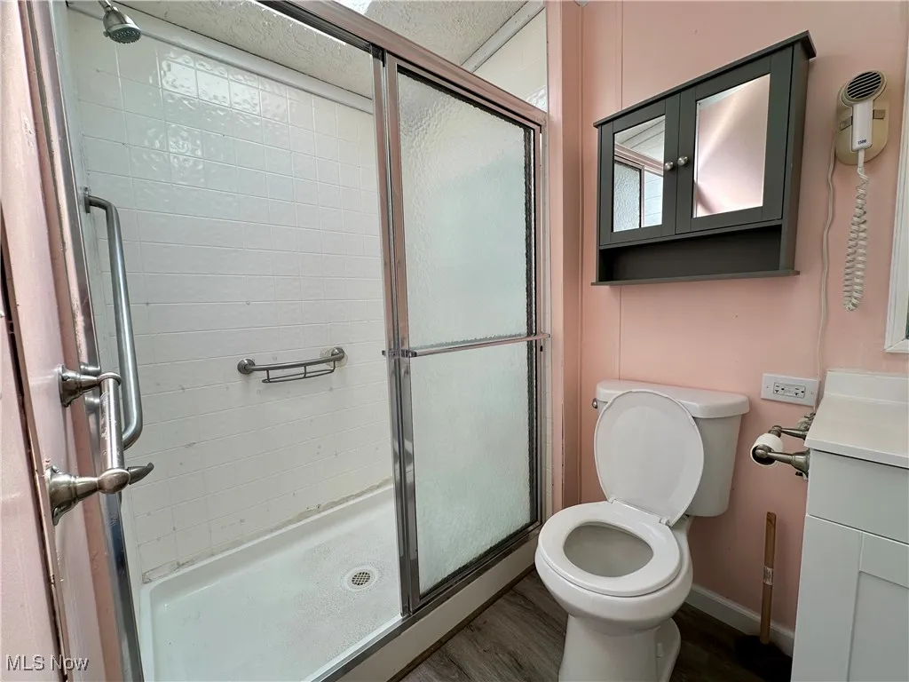 Full bath with a stall shower, vanity, toilet, baseboards, and wood finished floors