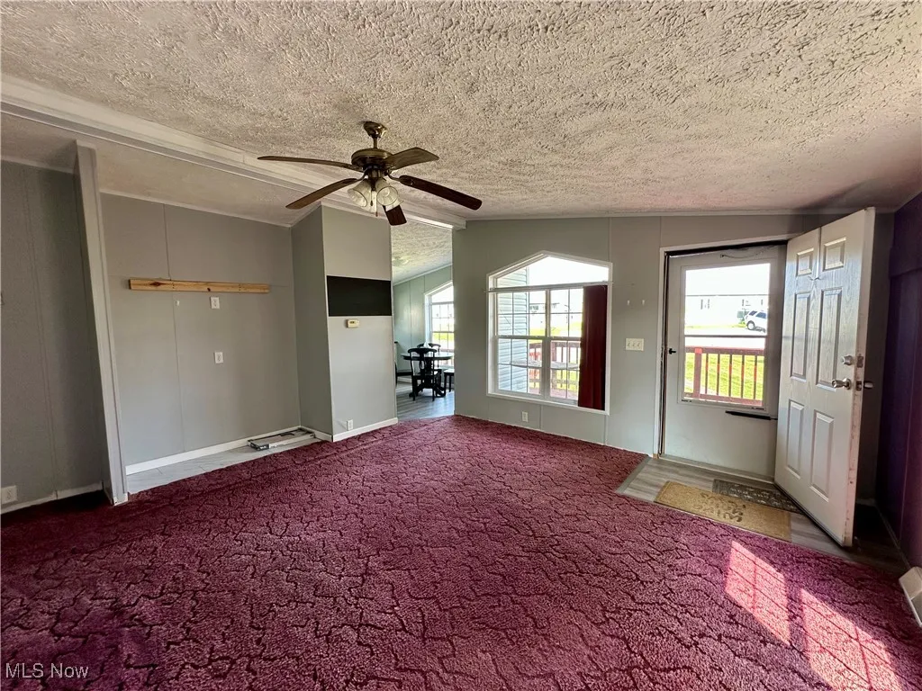 Carpeted entryway with a ceiling fan, vaulted ceiling, and a textured ceiling