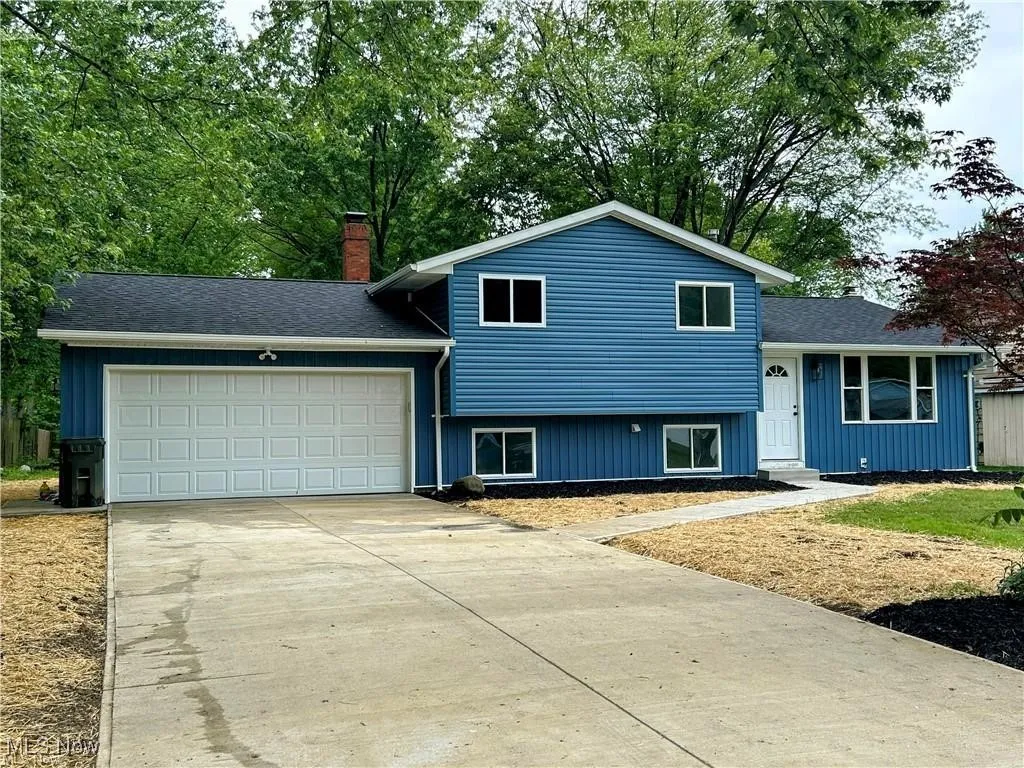 Tri-level home featuring a chimney, a garage, concrete driveway, board and batten siding, and roof with shingles