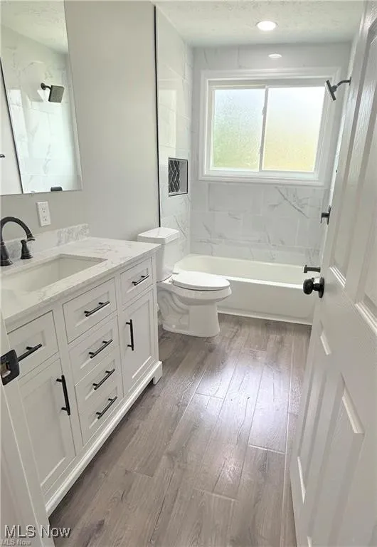 Bathroom featuring vanity, shower / bath combination, wood finished floors, and a textured ceiling