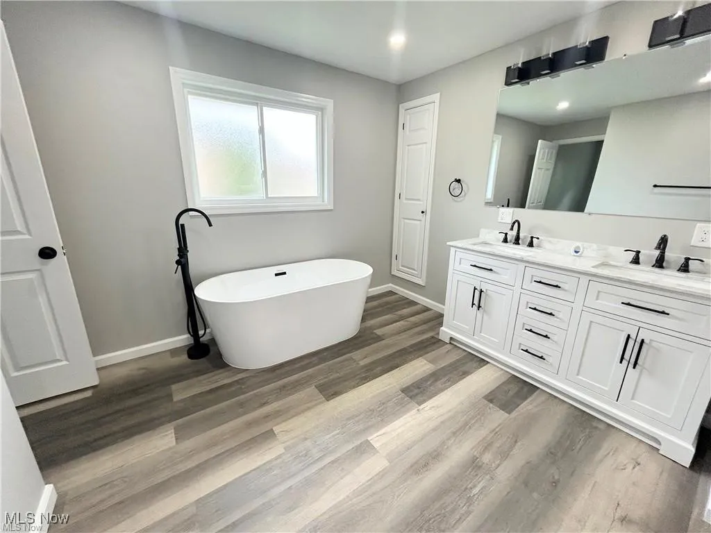 Full bathroom with double vanity, a soaking tub, and wood finished floors