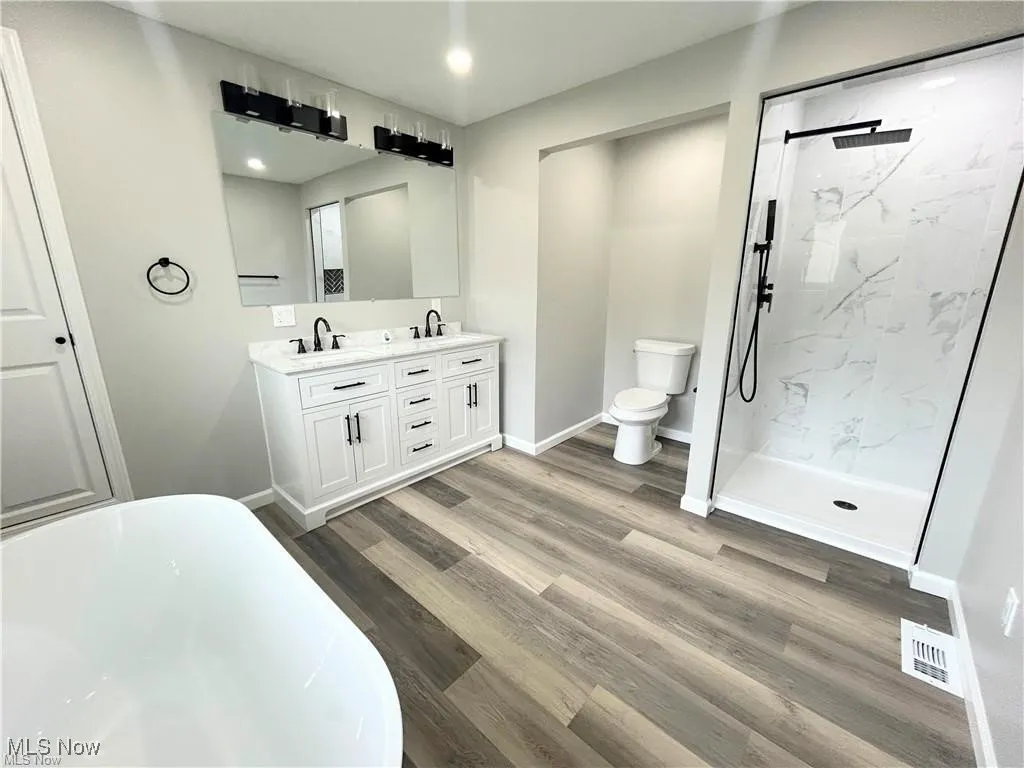 Bathroom featuring a freestanding bath, double vanity, a marble finish shower, and wood finished floors