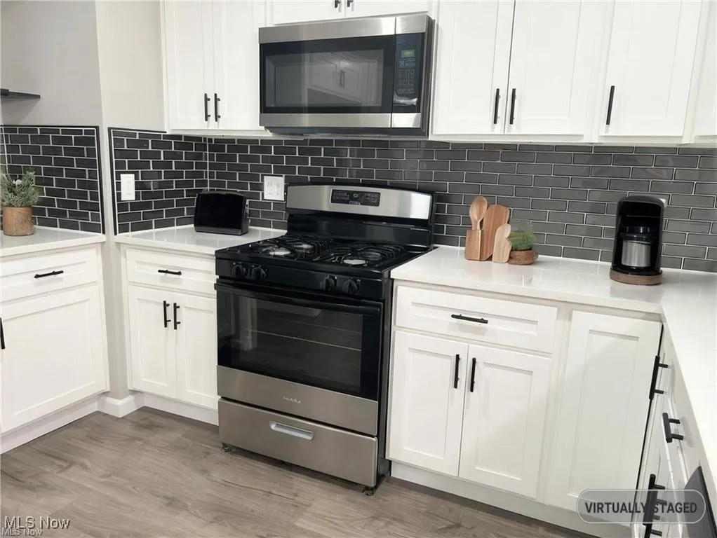 Kitchen with appliances with stainless steel finishes, white cabinets, light wood finished floors, and light countertops