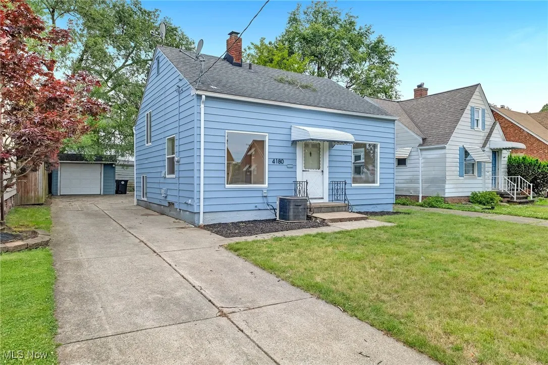 View of front of home with a chimney, an outbuilding, a front yard, roof with shingles, and a garage