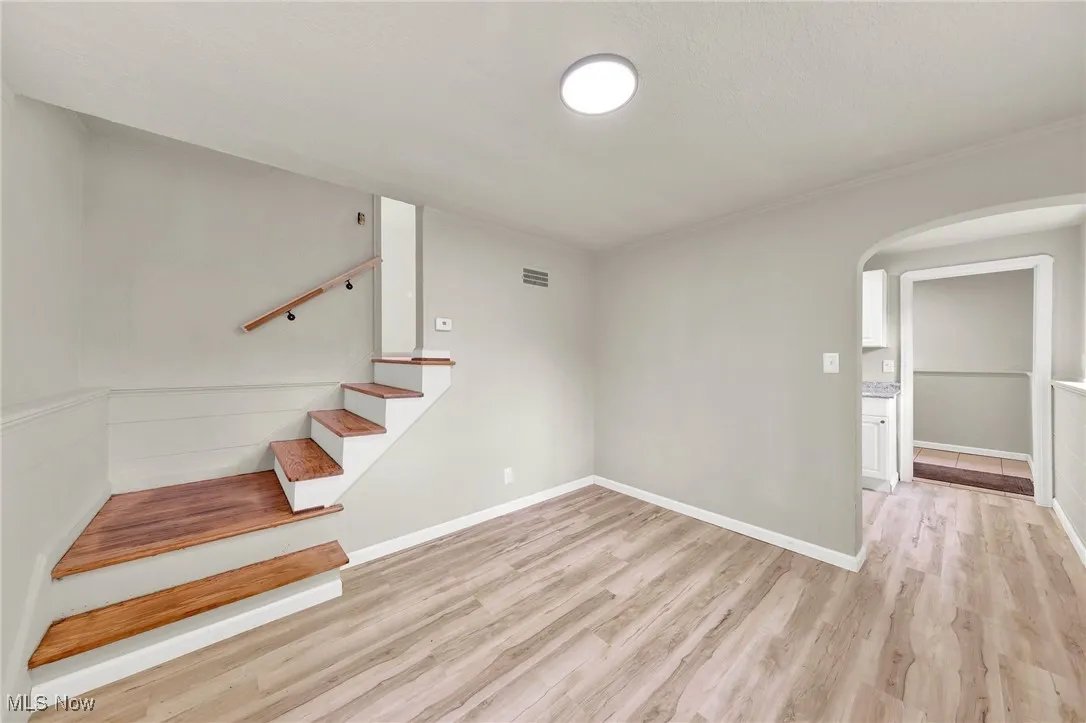 Stairs with arched walkways, wood finished floors, and crown molding