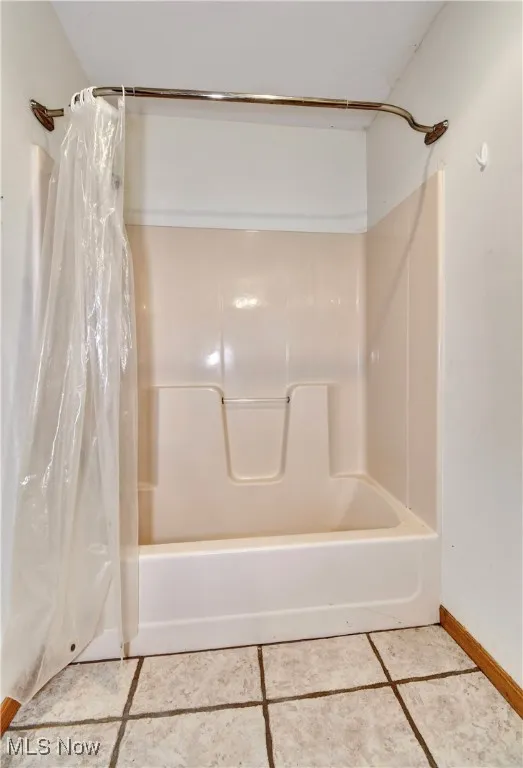 Bathroom featuring shower / bathtub combination with curtain and tile patterned flooring