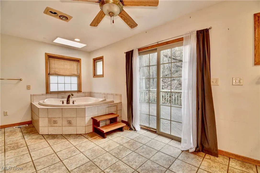 Full bath featuring a garden tub, a skylight, tile patterned floors, and ceiling fan