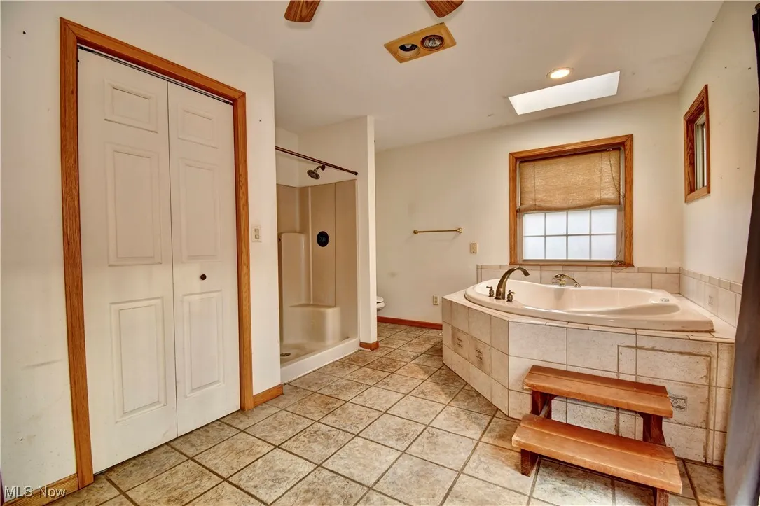 Bathroom with a skylight, a bath, tile patterned flooring, a shower stall, and a closet