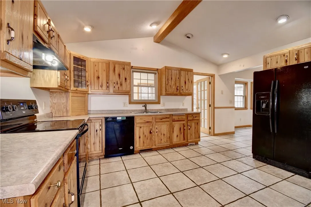 Kitchen featuring black appliances, under cabinet range hood, light tile patterned floors, light countertops, and glass insert cabinets