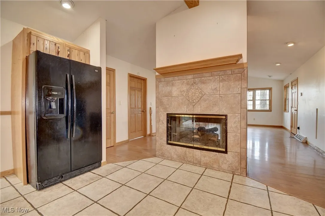 Kitchen featuring black refrigerator with ice dispenser, lofted ceiling, a fireplace, light brown cabinets, and light wood finished floors