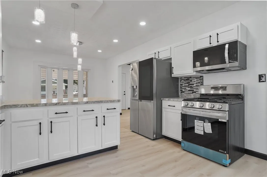 Kitchen with appliances with stainless steel finishes, light wood finished floors, white cabinetry, backsplash, and recessed lighting