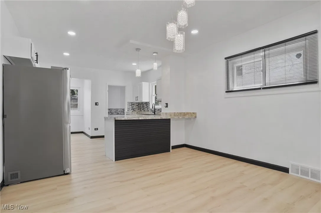Kitchen featuring freestanding refrigerator, light wood-style floors, white cabinets, a peninsula, and recessed lighting