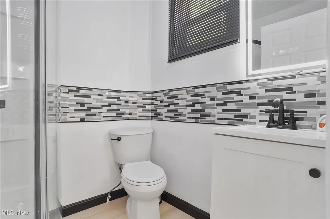 Bathroom featuring vanity, decorative backsplash, wood finished floors, and a shower