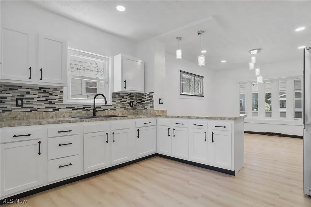 Kitchen with a peninsula, light wood-type flooring, decorative backsplash, recessed lighting, and white cabinets