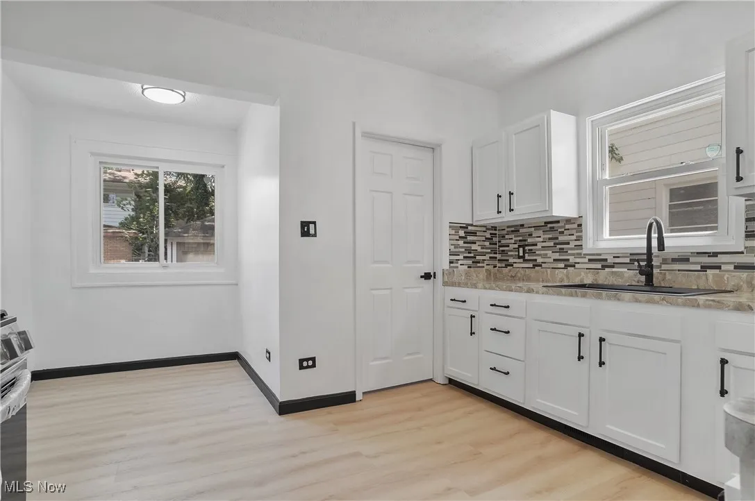 Kitchen with light wood-style flooring, decorative backsplash, white cabinets, and light stone counters