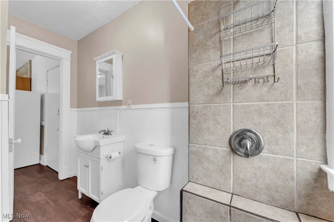 Full bathroom with wainscoting, vanity, a shower, and wood finished floors