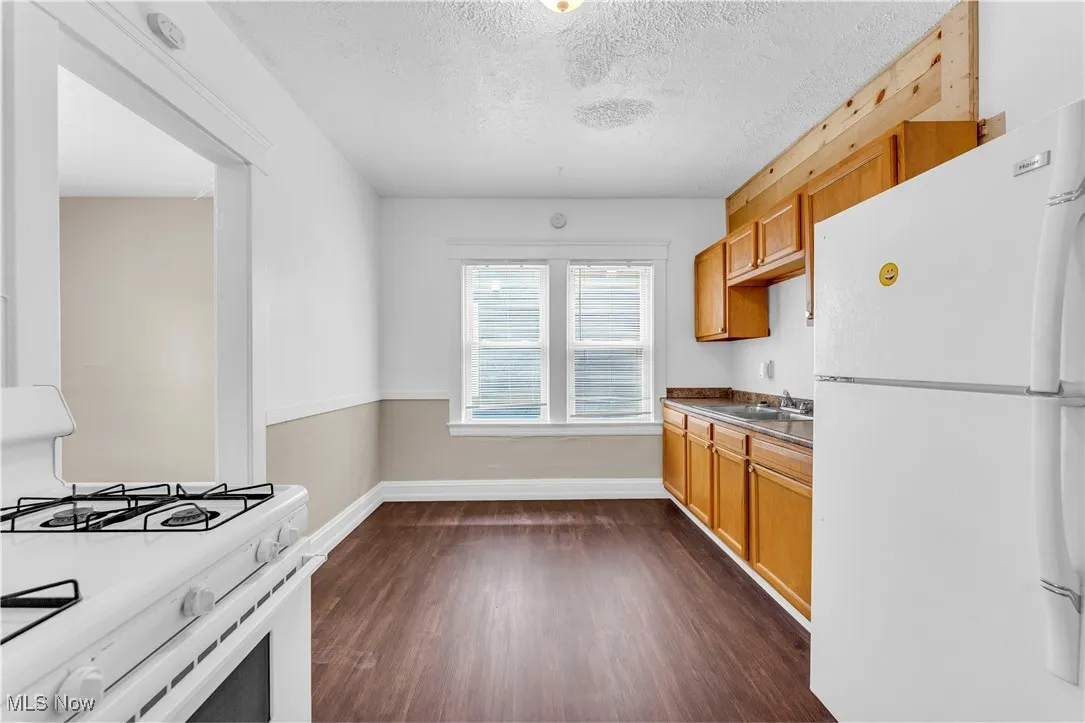Kitchen with white appliances, dark wood-style flooring, a textured ceiling, dark countertops, and brown cabinets