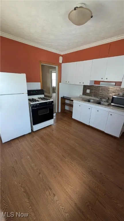 Kitchen featuring freestanding refrigerator, range with gas stovetop, backsplash, white cabinets, and dark wood-type flooring